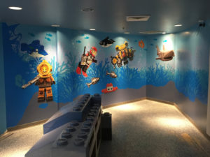 Wall wrapped with graphics of underwater lego scene, complete with minifig divers and lego fish, whales, and sharks